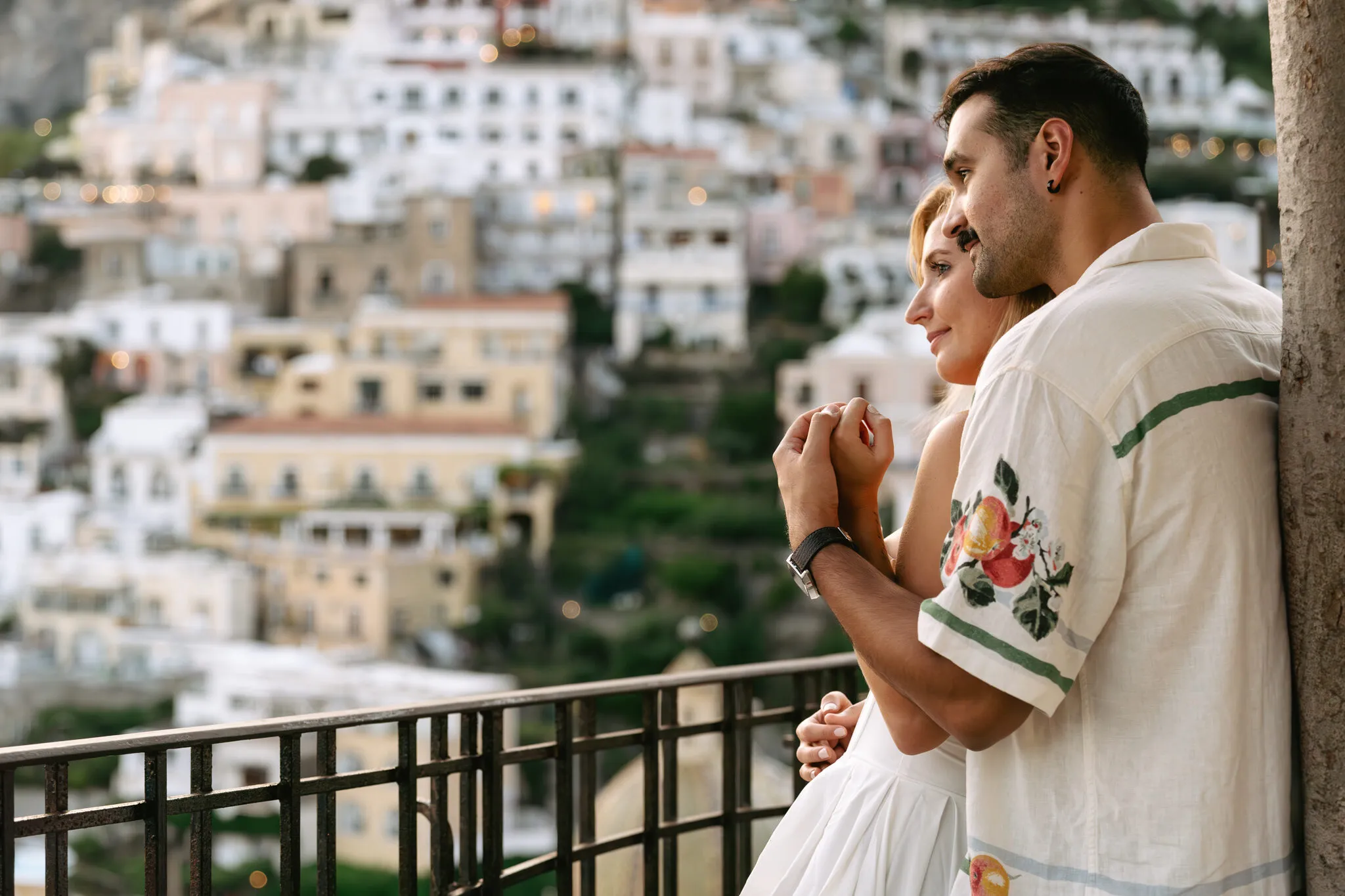 Couple embracing on a balcony overlooking the hillside town of Positano, Italy